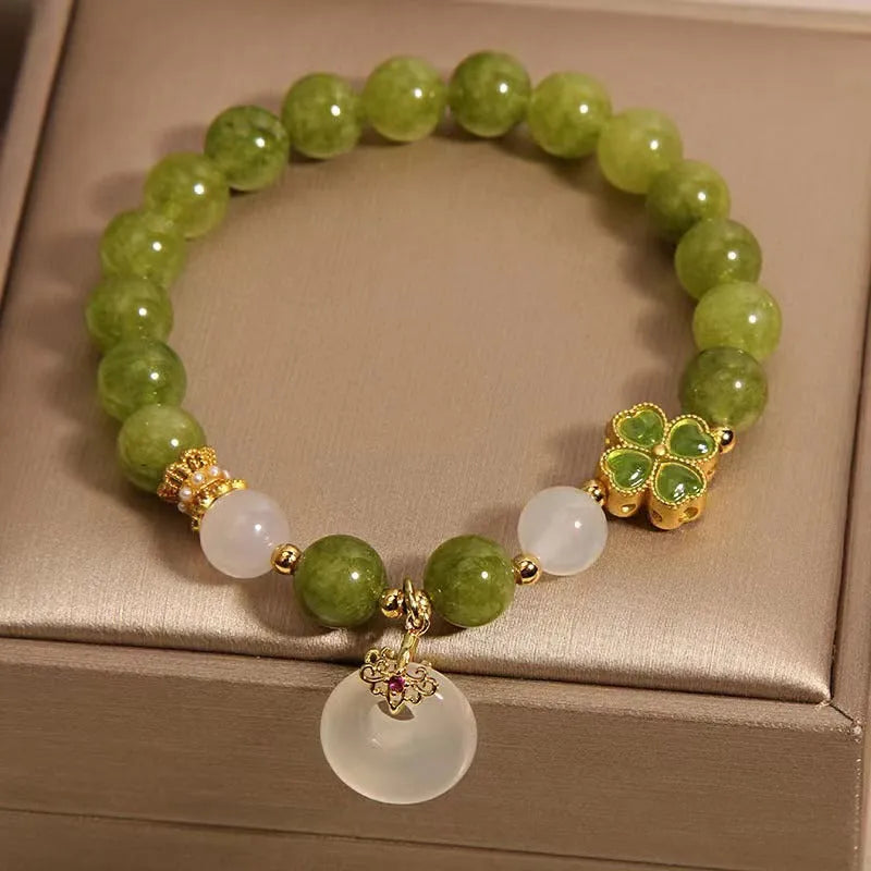 Women's green tourmaline bracelet with four-leaf clover charm and geometric drop pendant on a safety buckle.