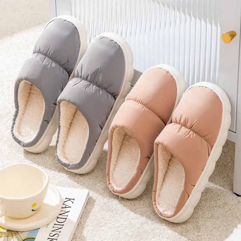 A pair of blue down cotton slippers with a thick rubber sole and artificial leather upper on a wooden floor.