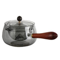 Semi-automatic rotary heat-resistant glass teapot with infuser and wooden handle on a table, transparent or grey