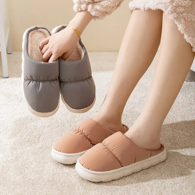A pair of blue down cotton slippers with a thick rubber sole and artificial leather upper on a wooden floor.