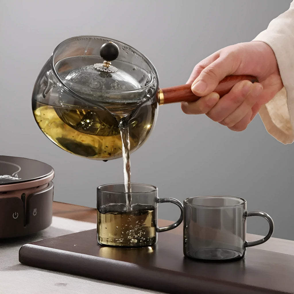 Semi-automatic rotary heat-resistant glass teapot with infuser and wooden handle on a table, transparent or grey