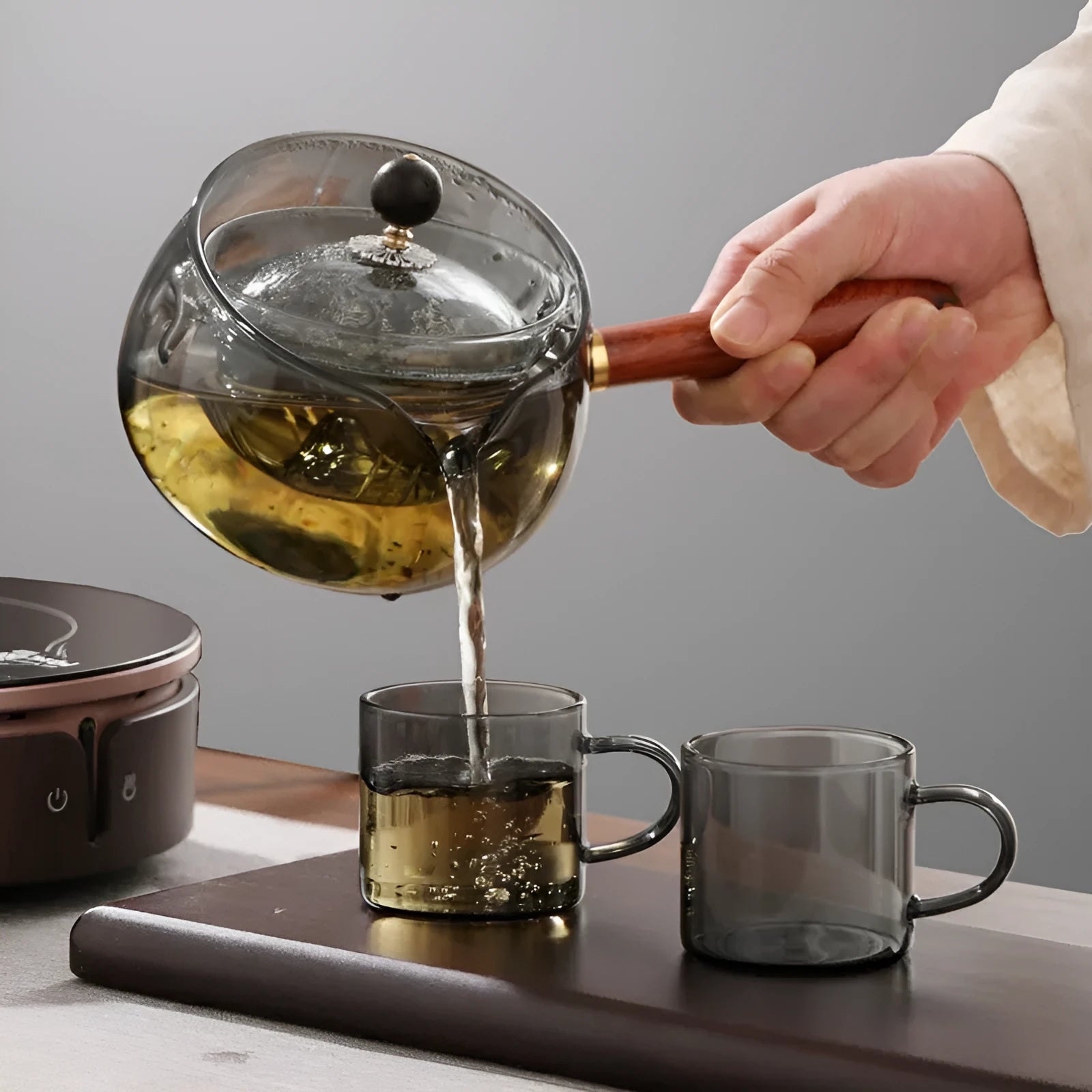 Semi-automatic rotary heat-resistant glass teapot with infuser and wooden handle on a table, transparent or grey
