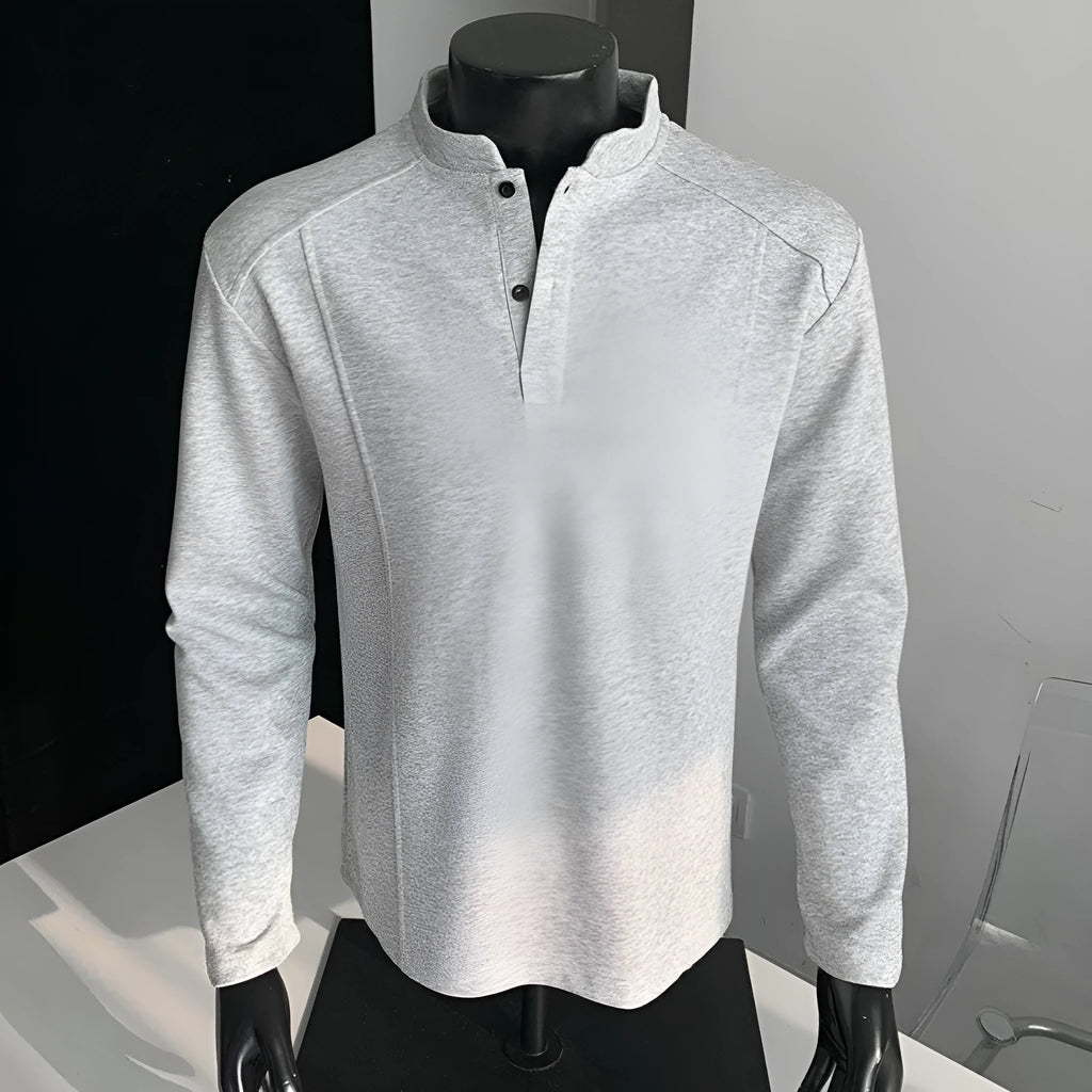 Man wearing a loose fit grey long sleeve sweater with an asymmetric design and a stand-up polo shirt collar.