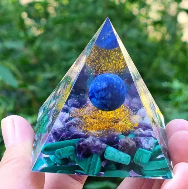 A 6cm high clear resin pyramid ornament filled with colourful crystal gravel on a wooden surface.