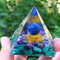A 6cm high clear resin pyramid ornament filled with colourful crystal gravel on a wooden surface.