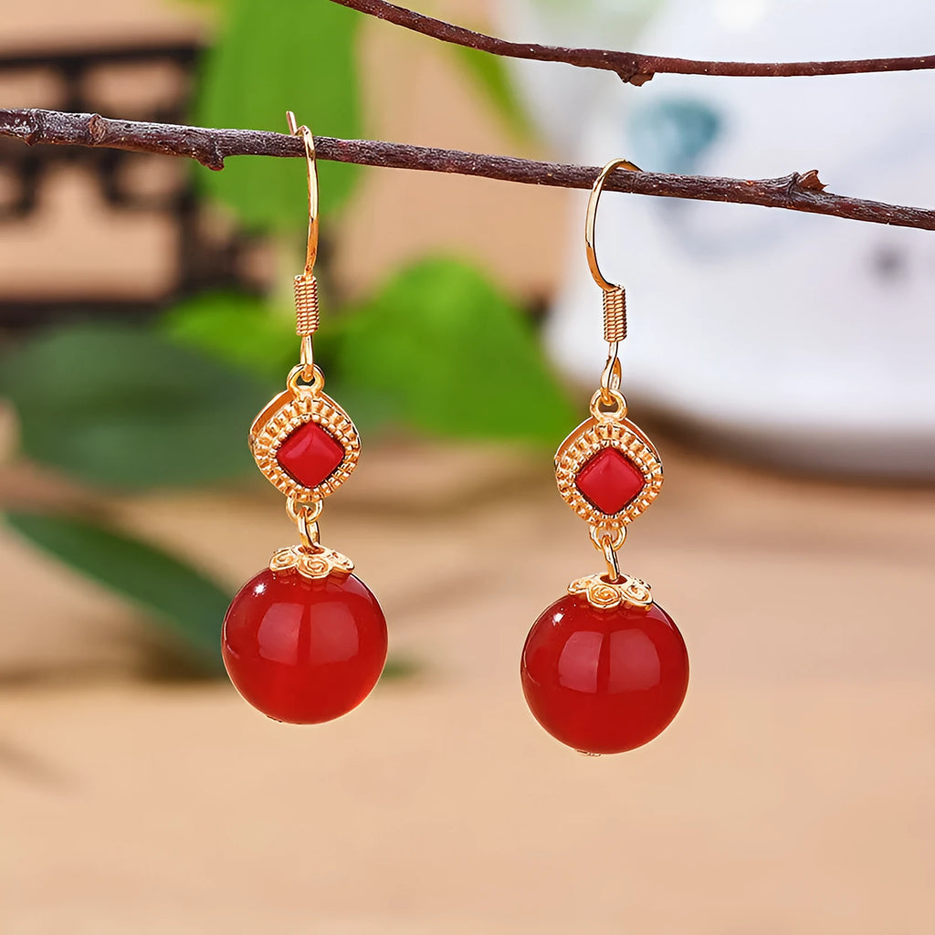 Round red agate bead drop earrings with silver-inlaid jasper accents on a geometric copper alloy hook.