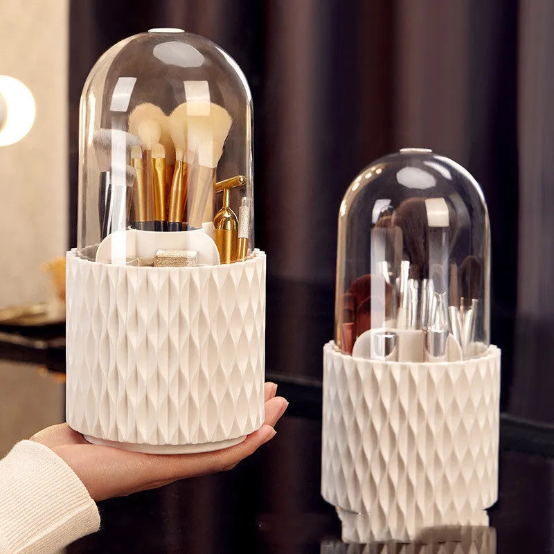 White acrylic rotating makeup brush holder with transparent body and a grey dust cover on a desk.