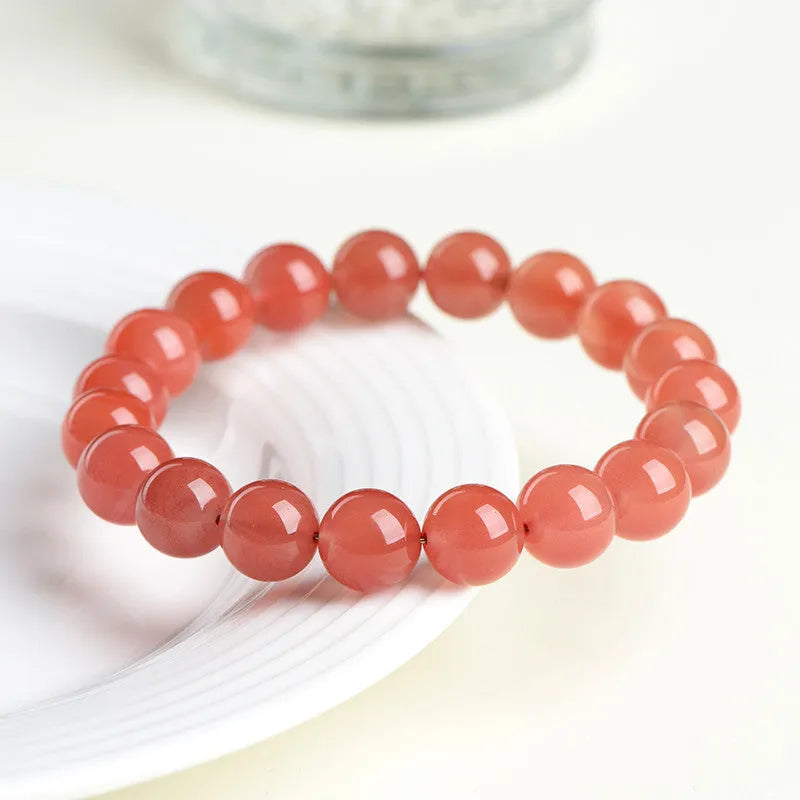 Natural cherry red agate bead bracelet on a wrist, showing polished stones and string construction.