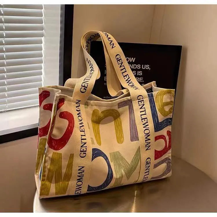 Large canvas tote shoulder bag with printed design in black letter, coloured letter, and pattern styles.