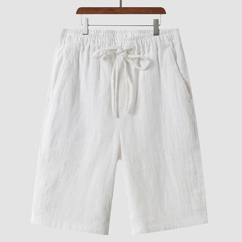 A pair of men's beige linen shorts with a loose, cropped cut and a mid-rise elasticated waistband.