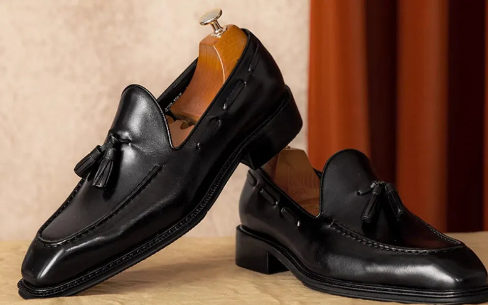 Men's black genuine leather slip-on loafers with fringed detailing and a rubber sole, shown from a side view.