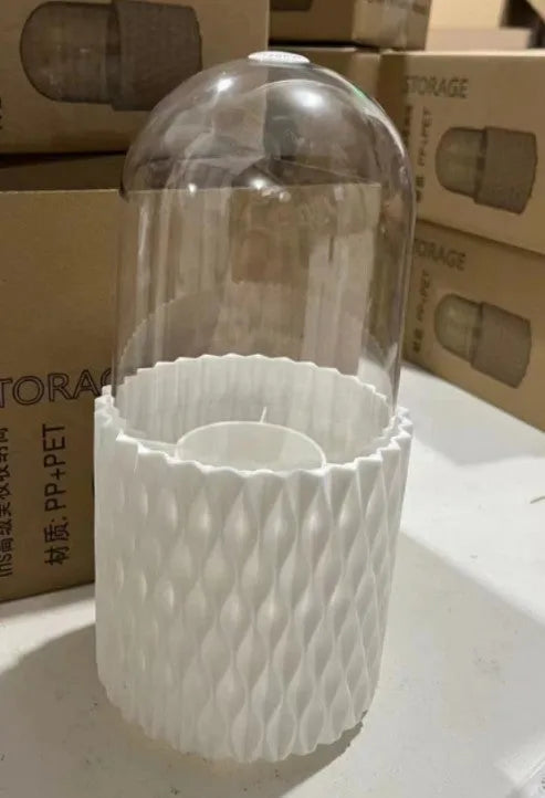 White acrylic rotating makeup brush holder with transparent body and a grey dust cover on a desk.