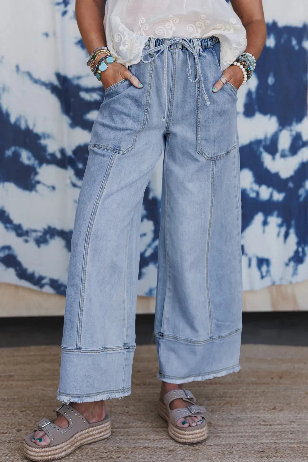 Beau blue women's wide leg denim trousers with a drawstring waistband and raw hem detail laid flat.