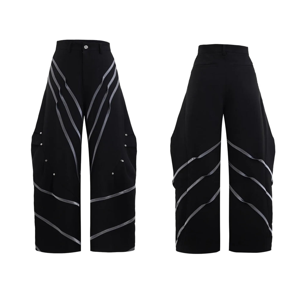 Men's black trousers with three-dimensional cut, metal striped rivet details and pleats on a white background.