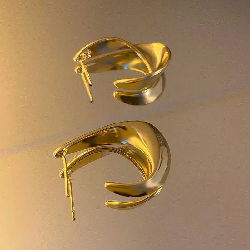Gold and silver twisted geometric metal earrings with a round design element.