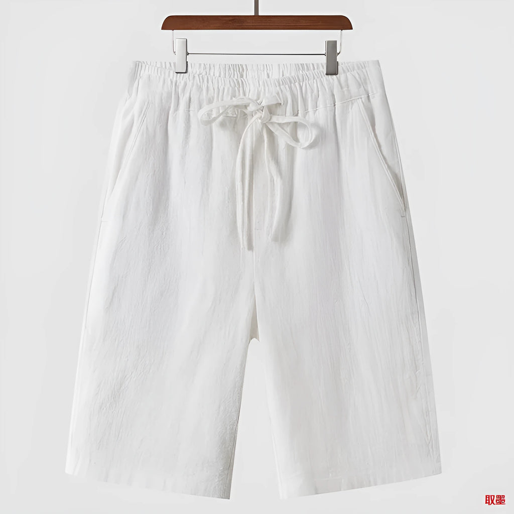 A pair of men's beige linen shorts with a loose, cropped cut and a mid-rise elasticated waistband.