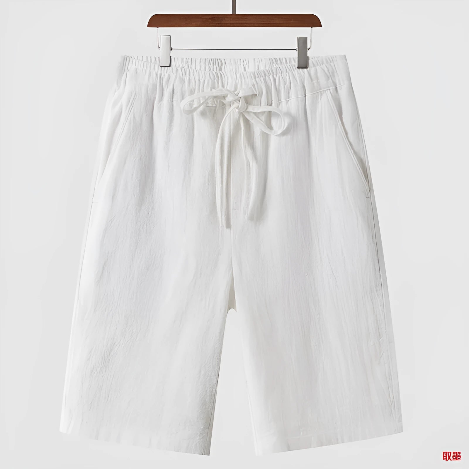 A pair of men's beige linen shorts with a loose, cropped cut and a mid-rise elasticated waistband.