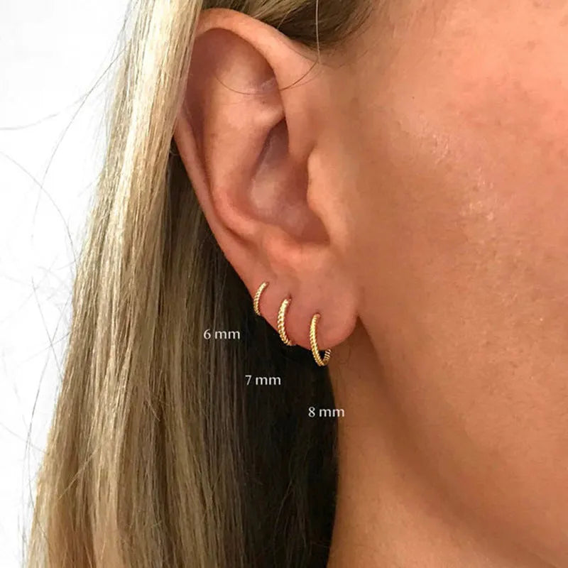 Twisted round sterling silver hoop earrings in golden and white gold colours on a plain background.