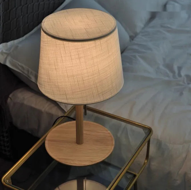 Walnut-coloured solid wood desk lamp with a white fabric shade on a wooden table.
