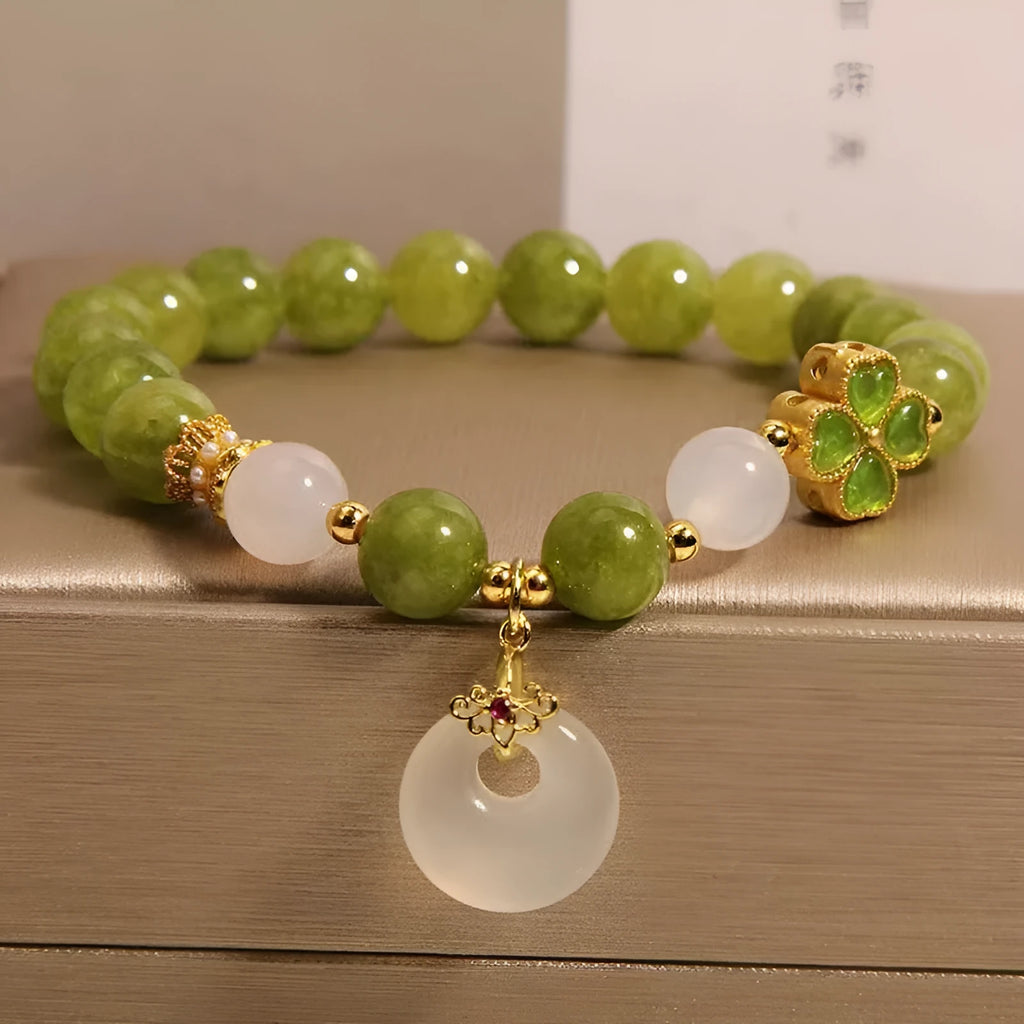 Women's green tourmaline bracelet with four-leaf clover charm and geometric drop pendant on a safety buckle.