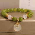 Women's green tourmaline bracelet with four-leaf clover charm and geometric drop pendant on a safety buckle.