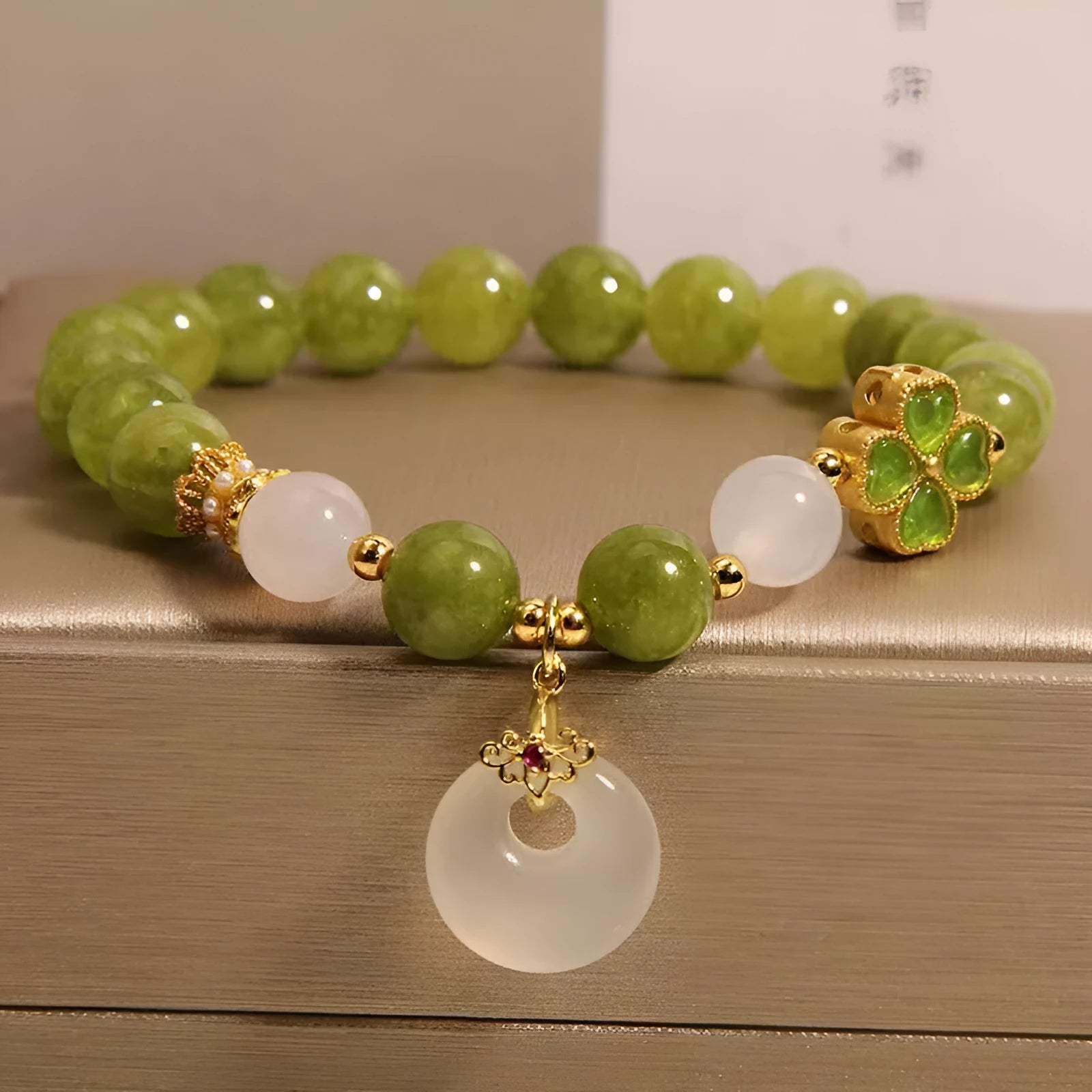 Women's green tourmaline bracelet with four-leaf clover charm and geometric drop pendant on a safety buckle.