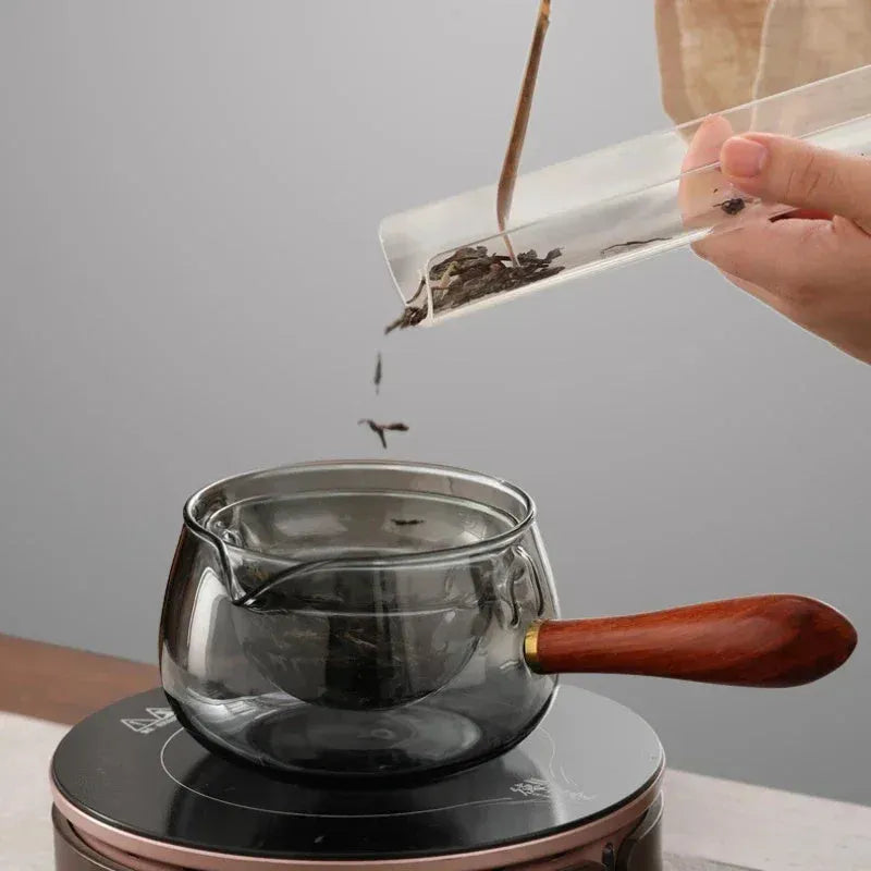 Semi-automatic rotary heat-resistant glass teapot with infuser and wooden handle on a table, transparent or grey