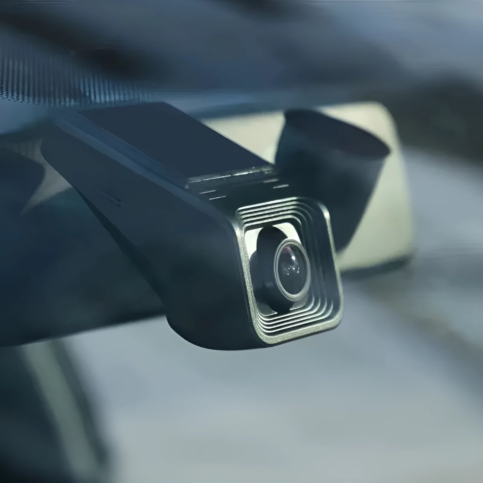 Black car dash cam mounted on windscreen with forward-facing lens and power cable
