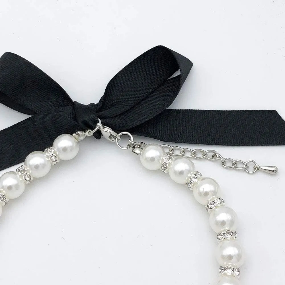 Small dog wearing blue pearl and rhinestone necklace with ribbon bow, adjustable clasp visible.