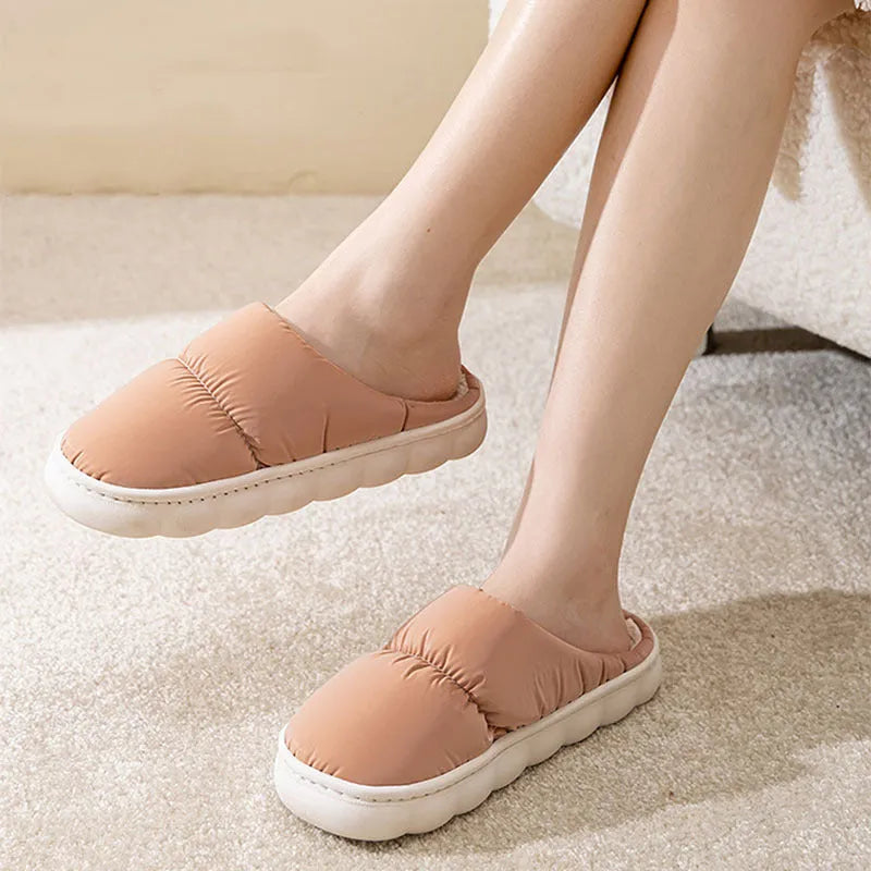 A pair of blue down cotton slippers with a thick rubber sole and artificial leather upper on a wooden floor.