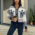 White women's jacquard cardigan with contrast stripes, zipper front, and lapel collar on a hanger.