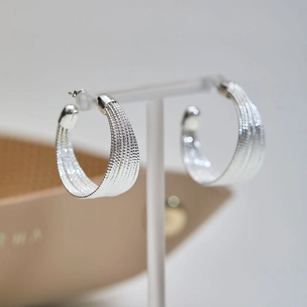 A pair of multi-layer geometric earrings in gold or silver electroplated finish, available as studs or clips.