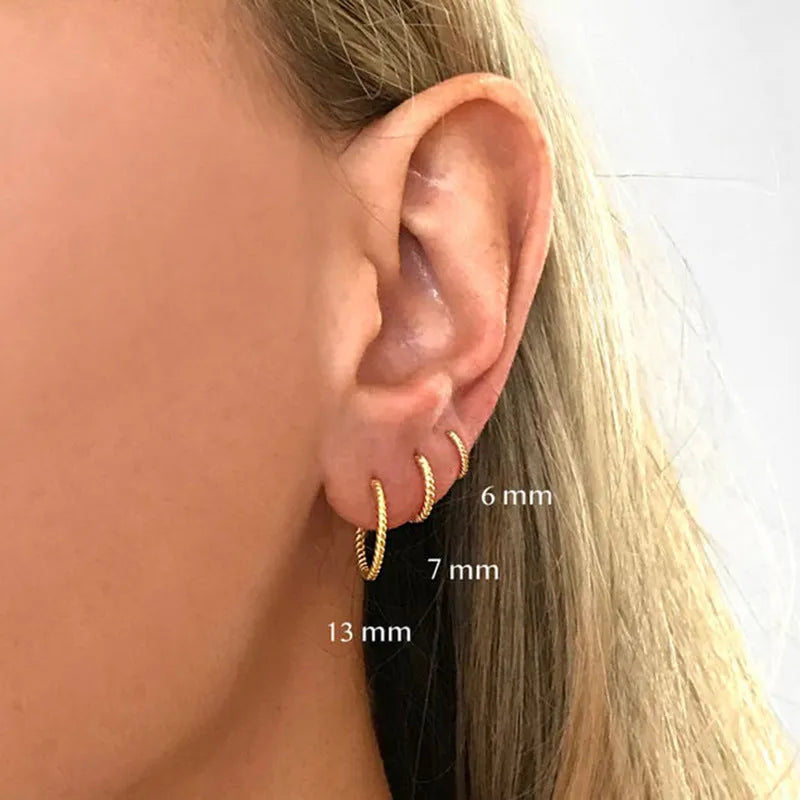 Twisted round sterling silver hoop earrings in golden and white gold colours on a plain background.
