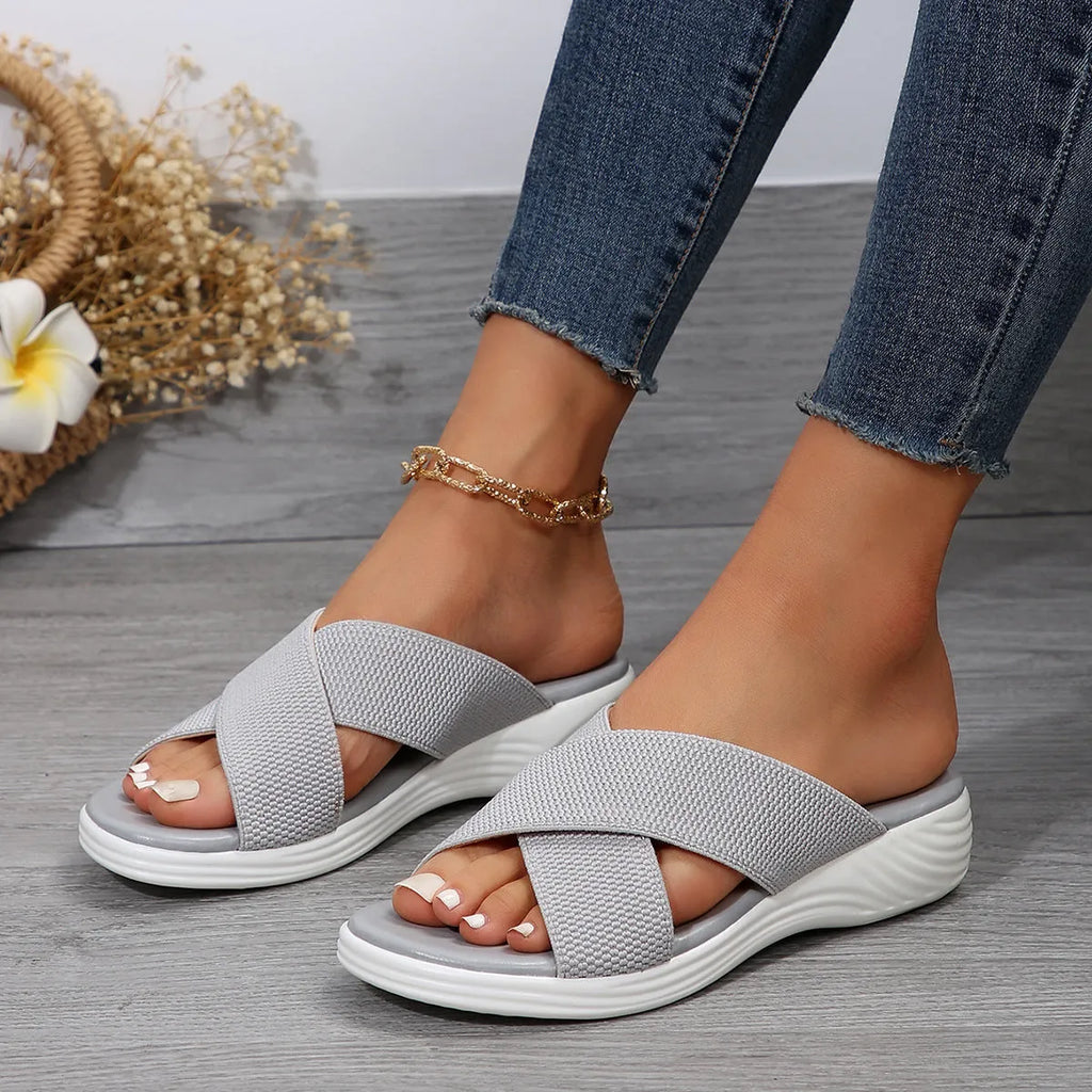 Women's black flat wedge slippers with peep toe and cross strap on a rubber sole.
