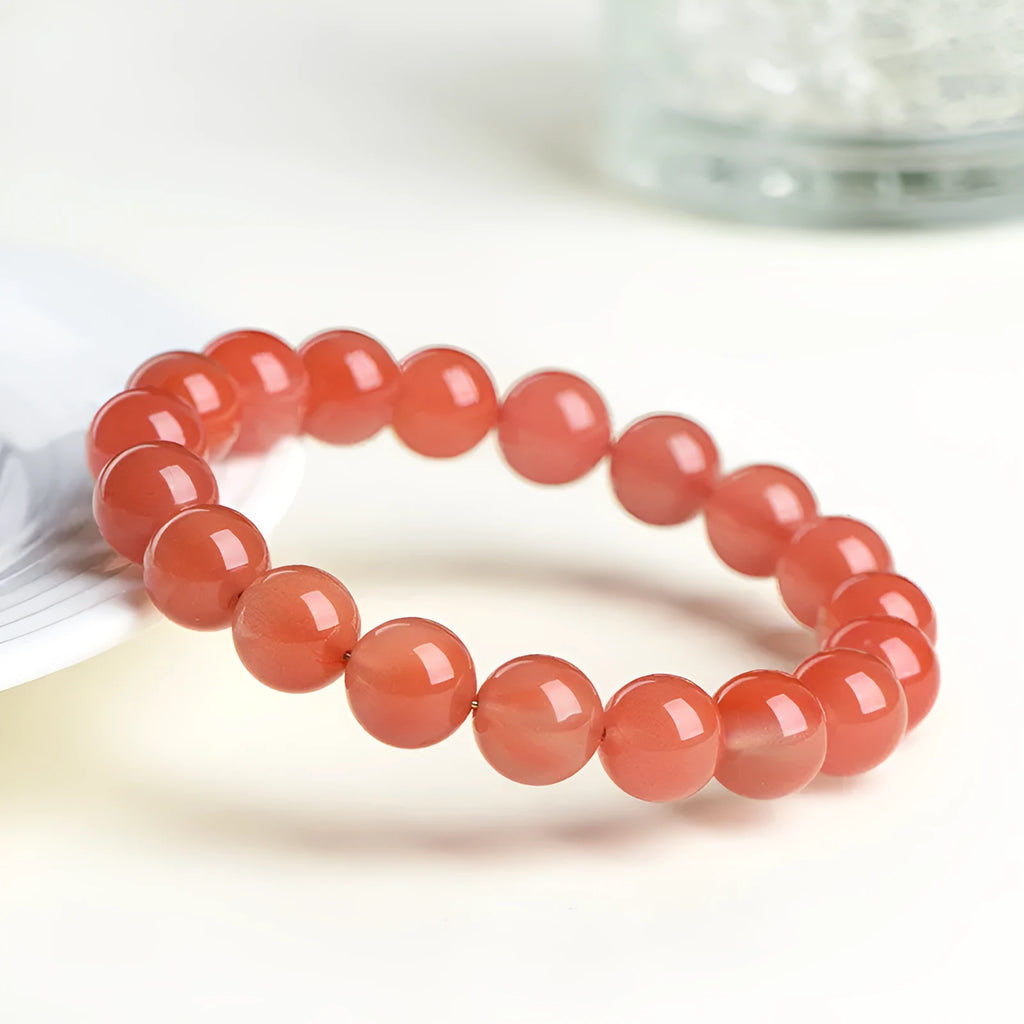 Natural cherry red agate bead bracelet on a wrist, showing polished stones and string construction.
