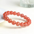 Natural cherry red agate bead bracelet on a wrist, showing polished stones and string construction.
