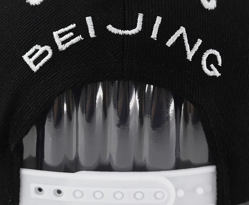 Black and white cotton baseball cap with letter embroidery on the front, showing adjustable strap.