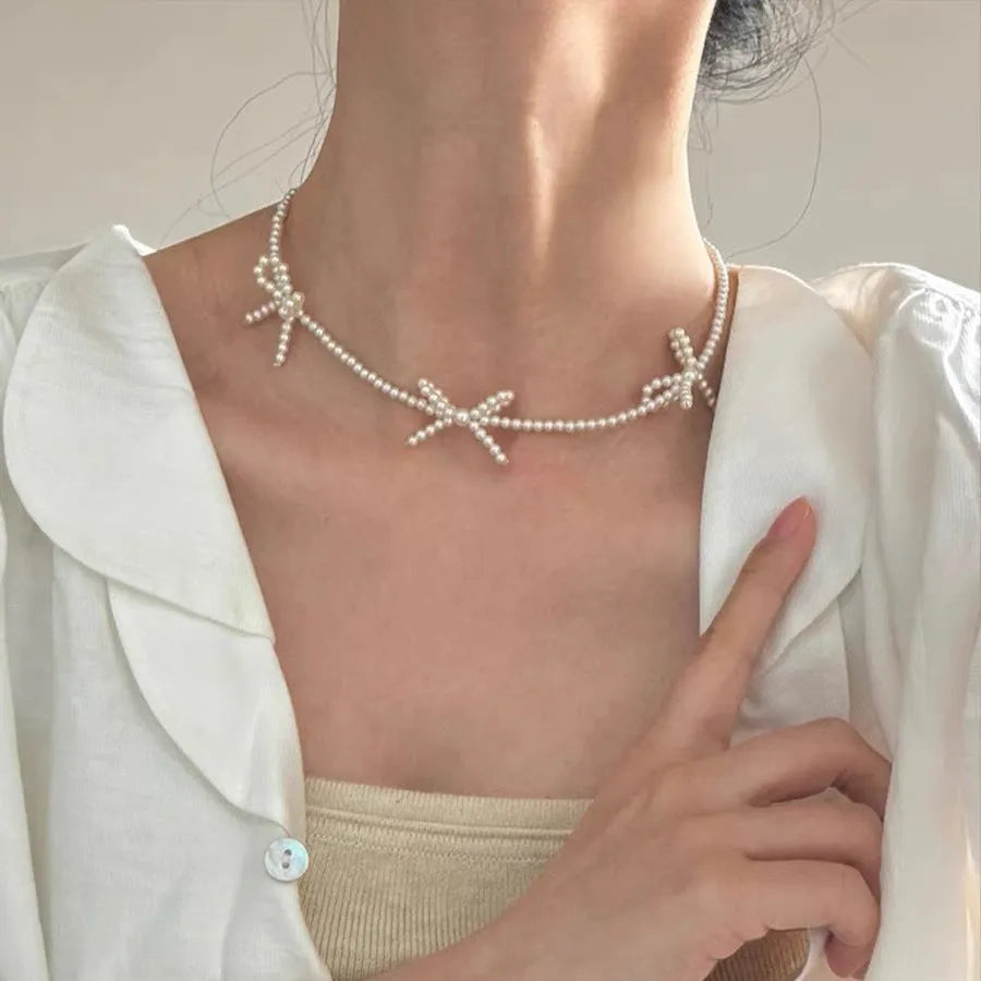 Women's white bow-shaped imitation pearl necklace with an adjustable chain.